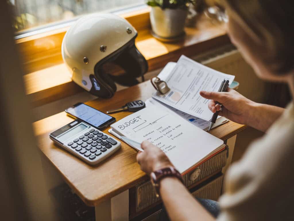 אדם יושב בבית ומסדר תקציב חודשי לצד קסדה ומפתחות קטנוע